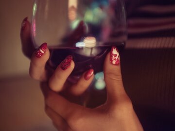 Nahaufnahme von rotlakierten Händen einer Frau, die ein Weinglas hält  | © Getty Images/Serdar Acar / EyeEm