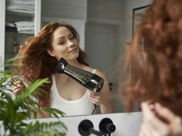 Frau föhnt sich die Haare vor dem Spiegel | © Getty Images/Anna Bizon / EyeEm