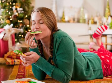 Frau isst Plätzchen vor Weihnachtsbaum | © Getty Images/Mark Edward Atkinson/Tracey Lee