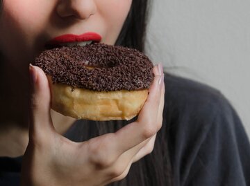 Frau mit roten Lippen beißt in einen Schoko-Donut | © Getty Images/Elizabeth Fernandez