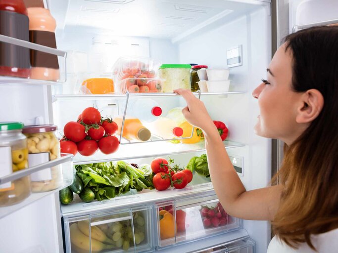Frau schaut in geöffneten Kühlschrank | © Getty Images/AndreyPopov