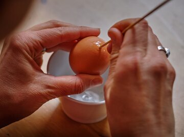Hände stechen ein Loch in Eierschalen, um Eier auszublasen. | © Getty Images/Jan Nevidal