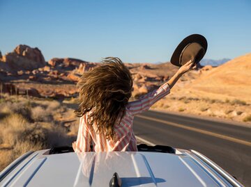 Frau im Auto und hält den Hut in einer Hand | © Getty Images/Jordan Siemens
