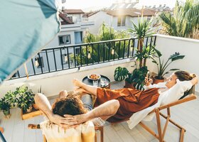Eine Frau liegt auf einem Liegestuhl auf ihrem Balkon inmitten von Pflanzen