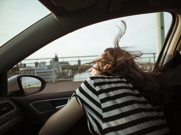 Frau streckt Kopf aus dem Autofenster | © Getty Images/Westend61