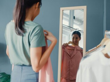 Frau wählt Klamotten vor Spiegel aus | © Getty Images/Tirachard