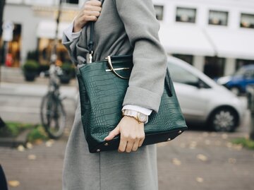 Aufnahme einer Frau, die einen grauen Mantel trägt und eine grüne Ledertasche über der Schulter | © Getty Images/Maskot