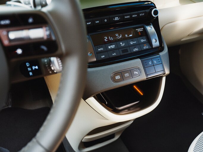 Nahaufnahme eines modernen Auto-Innenraums mit digitaler Klima- und Mediensteuerung, beleuchtetem Fach und cremefarbenem Armaturenbrett. | © Hyundai