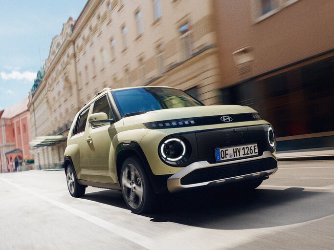 Ein hellgrüner SUV von Hyundai fährt dynamisch durch eine sonnige Altstadt mit historischen Fassaden und klarem Himmel. | © Hyundai
