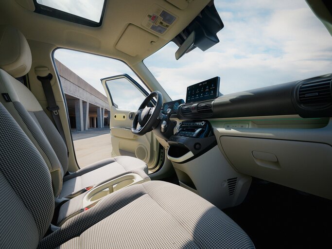 Moderner Autoinnenraum mit gemusterten Sitzen, großem Touchscreen-Display und offener Fahrertür, im Hintergrund ein sonniger Parkplatz. | © Hyundai