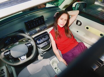Blick von oben auf eine Frau mit gelassenem Ausdruck, die in einem futuristischen Auto mit hellem Interieur sitzt. | © Hyundai