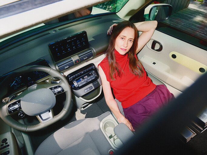Blick von oben auf eine Frau mit gelassenem Ausdruck, die in einem futuristischen Auto mit hellem Interieur sitzt. | © Hyundai