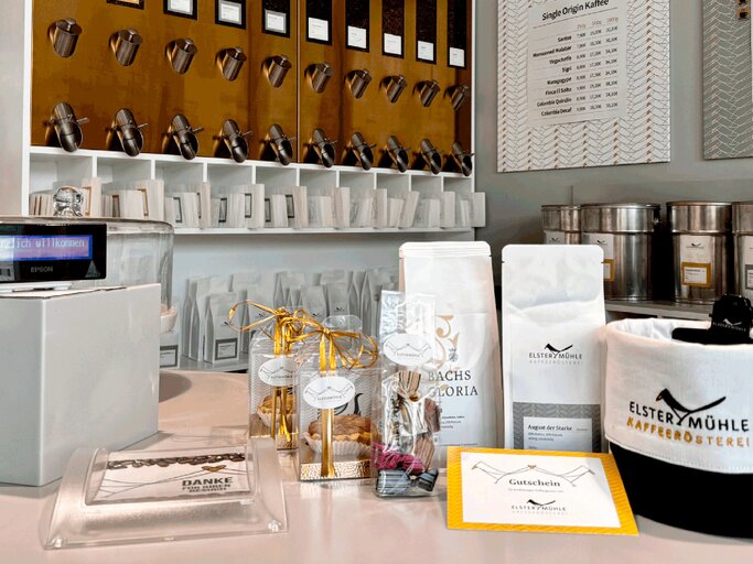 Verschieden verpackte Kaffees und Pralinen mit goldenen Schleifen stehen auf einer weißen Theke in stilvoller Kaffeerösterei. | © Marco Kitzing
