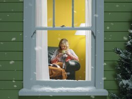 Frau liest vor dem Fenster ein Buch, draußen liegt Schnee, gemütliche Atmosphäre.  | © GettyImages/	Stephen Swintek