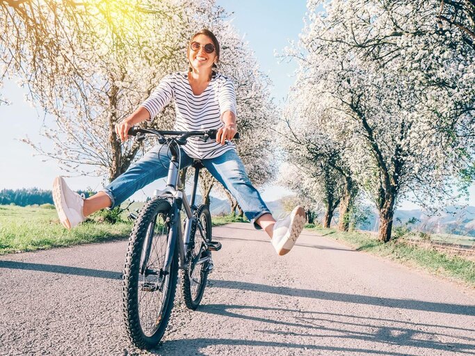 Person fährt Fahrrad durch blühende Allee | © Getty Images/Solovyova