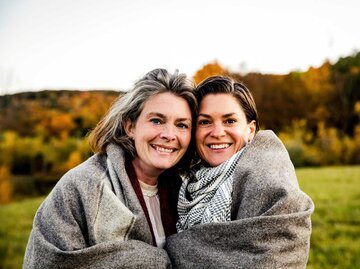 Zwei Frauen sind in einer Decke eingewickelt und lächeln in die Kamera | © Getty Images/The Good Brigade