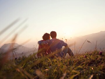 Paar sitzt bei Sonnenuntergang in Wiese | © Getty Images/Westend61