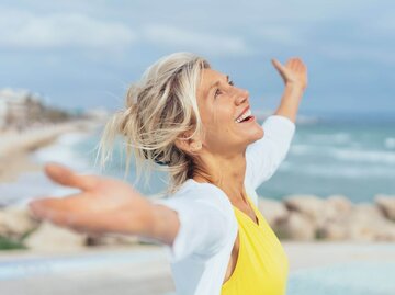 Person mit ausgebreiteten Armen und lachend im Sommer | © Getty Images/stockfour