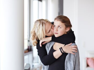 Eine Mutter umarmt ihre Tochter von hinten und diese schaut genervt | © GettyImages/Klaus Vedfelt