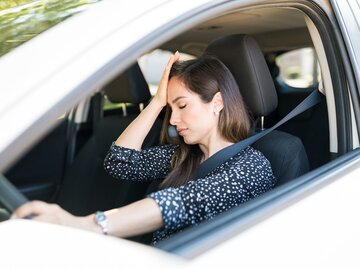 Eine Frau sitzt am Steuer ihres Autos und hat ihre Hand an der Stirn | © GettyImages/Antonio_Diaz