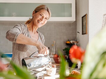 Eine Frau steht energiegeladen in der Küche und macht sich etwas zu trinken | © GettyImages/Westend61