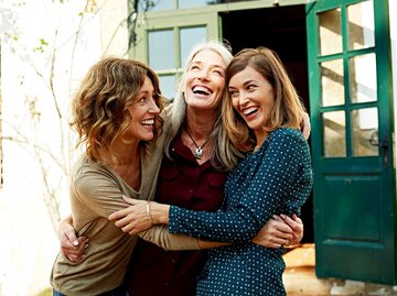 Drei Frauen umarmen sich freudig vor einem Haus. | © Getty Images / Morsa Images