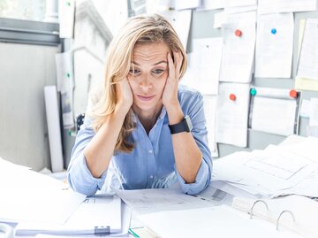 Frau sitzt verzweifelt vor zu viel Arbeit im Büro am Schreibtisch. | © Getty Images / Westend61