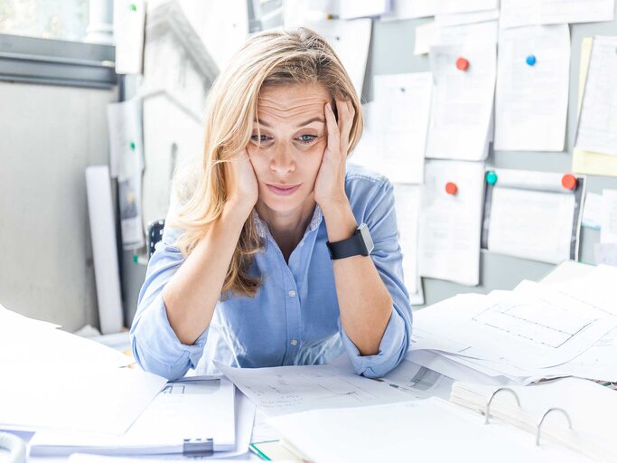 Frau sitzt verzweifelt vor zu viel Arbeit im Büro am Schreibtisch. | © Getty Images / Westend61