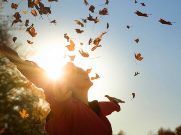 Frau wirft Herbstblätter in die Luft | © Getty Images/Westend61