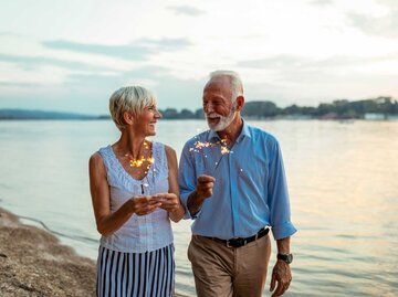 Älteres Paar läuft zusammen am See mit Wunderkerzen in der Hand. | © Adobe Stock/bernardbodo
