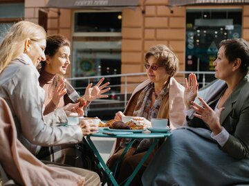 Gruppe von vier Freundinnen sitzt im Café am Tisch und unterhält sich. | © Adobe Stock/dsheremeta
