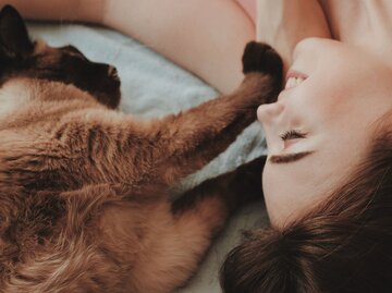 Frau liegt auf einem Bett und schmust mit ihrer Katze | © Unsplash/Oleg Ivanov