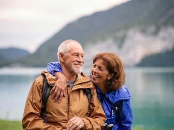 Älteres Paar steht glücklich an einem See. | © Adobe Stock/Halfpoint