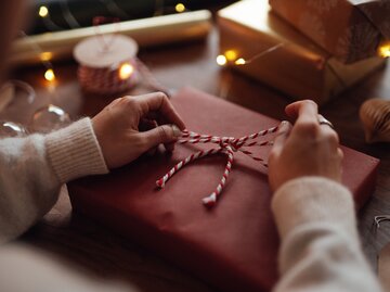 Hände machen eine Schleife um ein Geschenk | © GettyImages/Oscar Wong