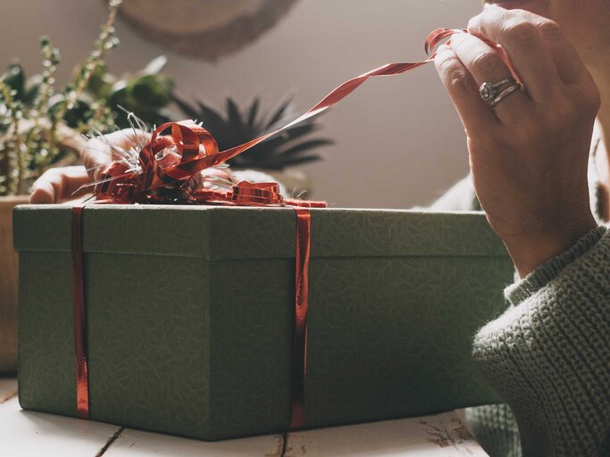 Die Hand einer Frau packt ein Geschenkebox aus. | © Adobe Stock/simona