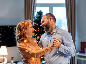 Frau und Mann tanzen in weihnachtlichem Ambiente | © Getty Images/ljubaphoto