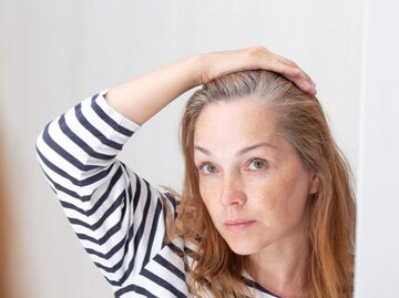 Person sieht sich grauen Haaransatz im Spiegel an | © Getty Images/Tatiana Foxy