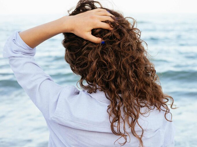 Frau greift sich von hinten in ihr lockiges Haar | © Getty Images/iprogressman