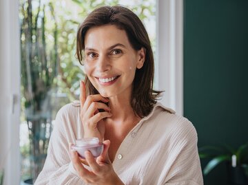 Eine Frau hält eine Creme in der Hand und cremt sich ein | © GettyImages/Westend61