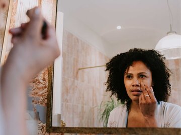Frau schminkt sich im Bad vor dem Spiegel | © Getty Images/Catherine Falls Commercial