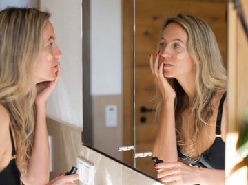 Frau schminkt sich im Bad vor dem Spiegel | © Getty Images/Kathrin Ziegler
