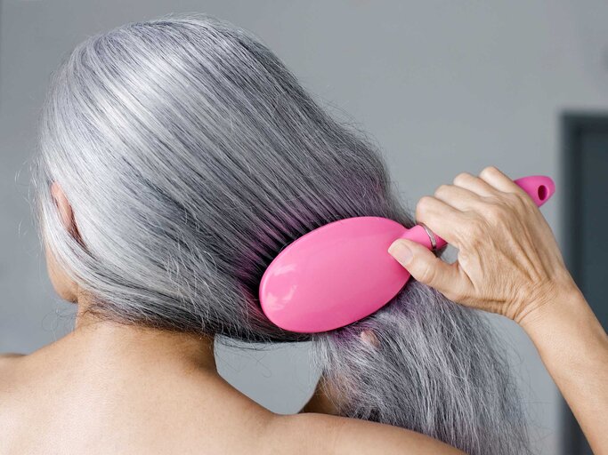 Frau kämmt ihre langen grauen Haare mit einer pinken Haarbürste. | © Getty Images / Patrik Giardino