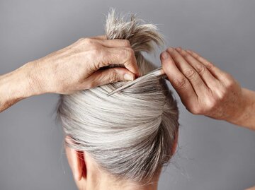 Frau mit grauen Haaren klammert sich die Haare hoch | © Getty Images/Maria Fuchs