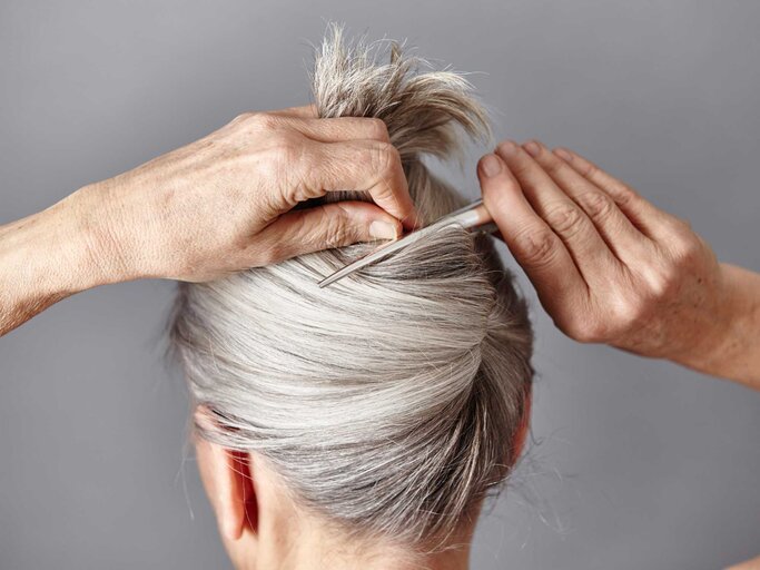 Frau mit grauen Haaren klammert sich die Haare hoch | © Getty Images/Maria Fuchs