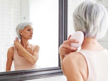 Frau kämmt sich und schaut dabei in den Spiegel | © Getty Images/Ekaterina Demidova