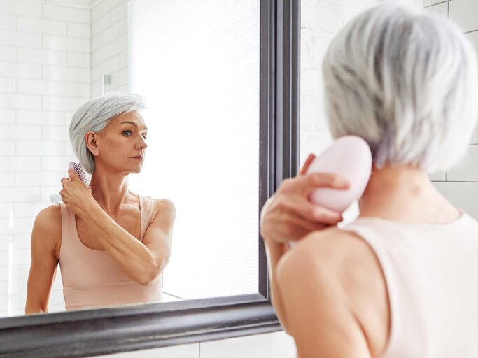 Frau kämmt sich und schaut dabei in den Spiegel | © Getty Images/Ekaterina Demidova
