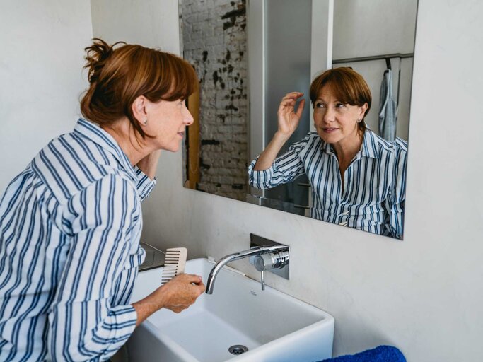 Ältere Frau betrachtet ihre Haare vor dem Spiegel | © Getty Images/urbazon
