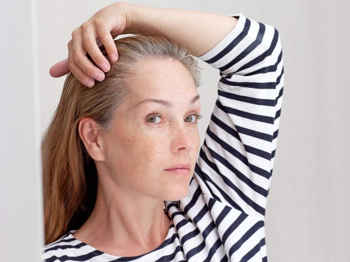 Person schaut sich grauen Haaransatz | © Getty Images/Tatiana Foxy