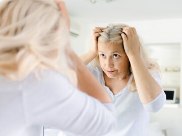 Eine Frau schaut ihre grauen Haare im Spiegel an | © GettyImages/RobertoDavid