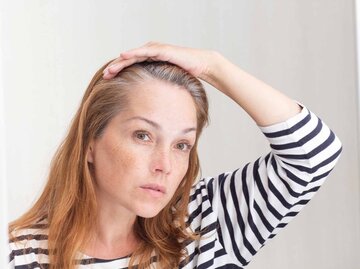 Frau betrachtet erste graue Haare im Spiegel | © Getty Images/Tatiana Foxy